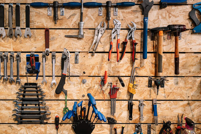 Várias ferramentas de metal penduradas em fileiras na parede de madeira em serviço de reparação de bicicletas degradadas — Fotografia de Stock