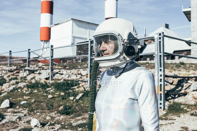 Side view spacesuit standing on rocky ground against metal fence and striped rocket shaped antennas on sunny day — Stock Photo