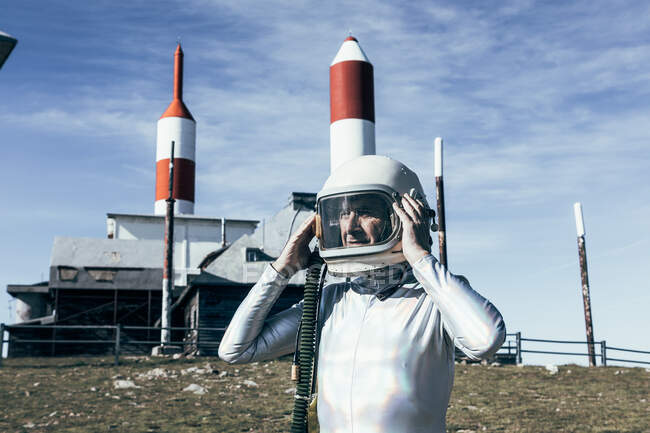 Homem em traje espacial em pé em solo rochoso contra cerca de metal e foguetes listrados em forma de antenas no dia ensolarado — Fotografia de Stock