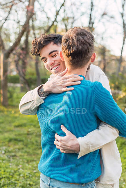 Cheerful LGBT couple of males embracing while standing in park on sunny day — Stock Photo