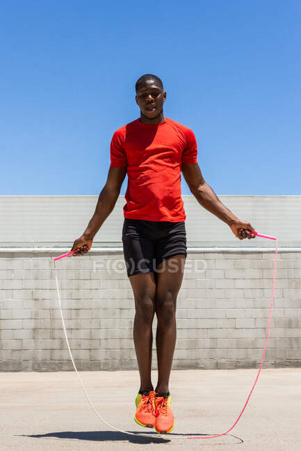 Energetic African American male athlete skipping rope above ground while doing exercises during training in summer — Stock Photo