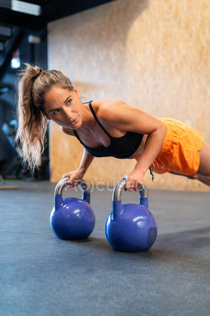 Entschlossene Sportlerin in Sportbekleidung in Plankenpose beim Functional Training mit Gewichten am Boden in der Turnhalle, die wegschauen — Stockfoto