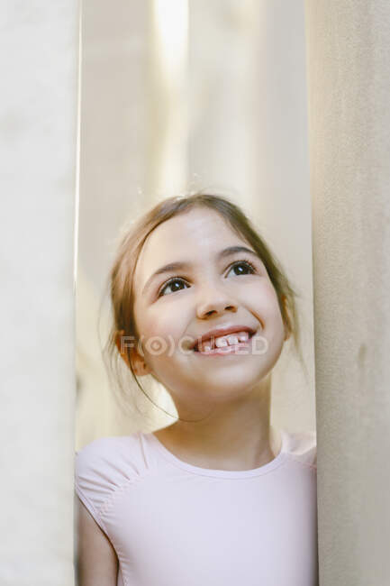 Positive cheerful girl in ballet uniform standing near stone column in park and looking away — Stock Photo