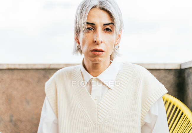 Stylische Transgender-Frau im trendigen Outfit sitzt im Sessel auf der Terrasse und blickt in die Kamera — Stockfoto