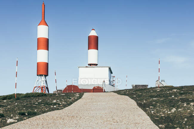 Edifici industriali con antenne a forma di razzo a strisce situate vicino al sentiero contro il cielo blu senza nuvole — Foto stock