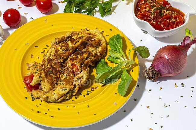 Köstliche Omelette mit gehackter Petersilie auf Teller gegen sonnengetrocknete Tomaten und rohe rote Zwiebel auf weißem Hintergrund — Stockfoto