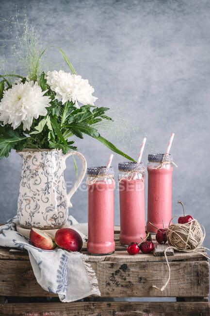 Освіжаючий молочний коктейль з нектаринами і вишнею подається в окулярах на дерев'яному столі з квітами — стокове фото
