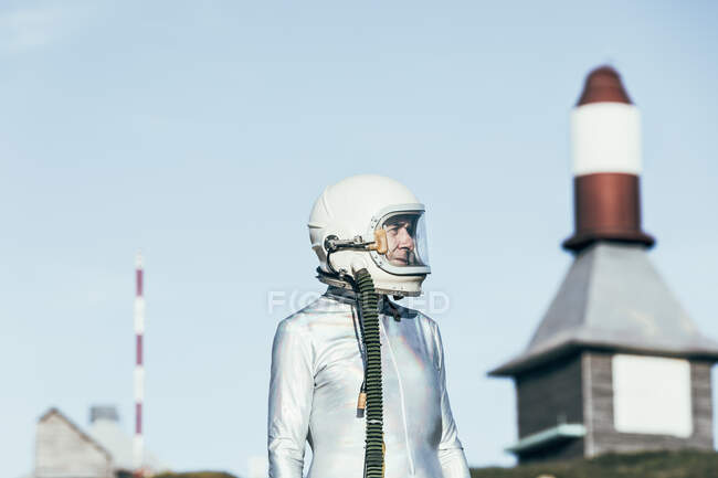 Homme en combinaison spatiale debout sur un sol rocheux contre des antennes rayées en forme de fusée par une journée ensoleillée — Photo de stock