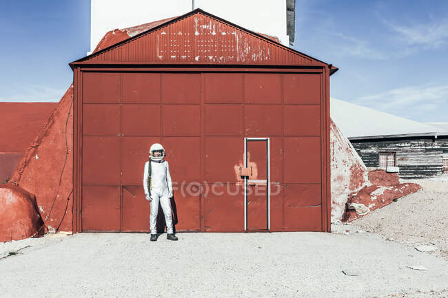 Man in spacesuit standing near red wall of industrial facility on sunny day — Stock Photo