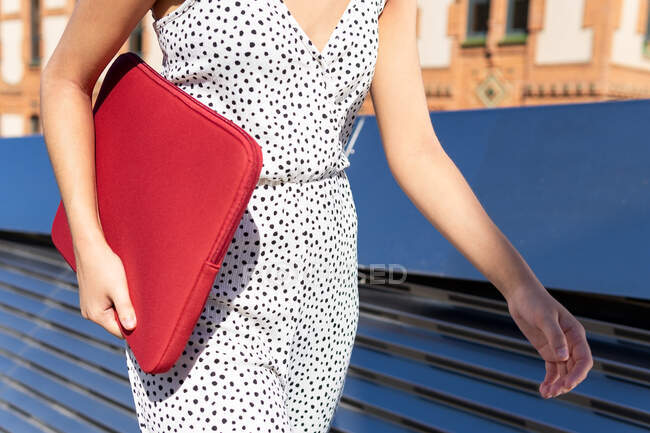 Crop view of anonymous woman carrying a red laptop case while walking on a sunny summer day — Stock Photo
