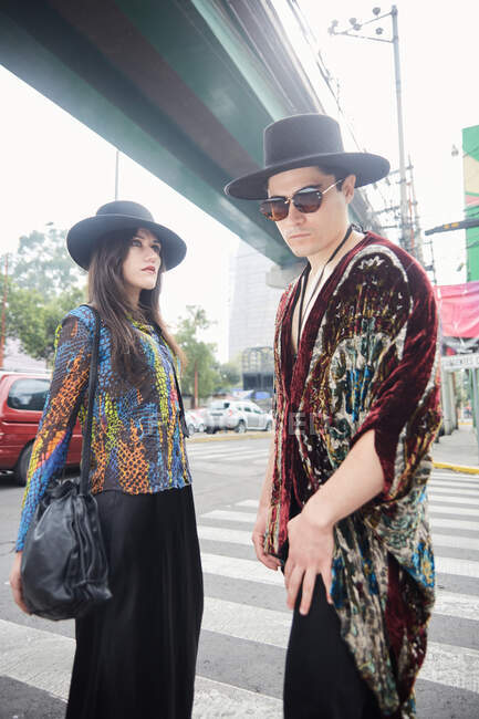 Vue latérale du couple élégant confiant en vêtements hipster debout sur la rue en été — Photo de stock