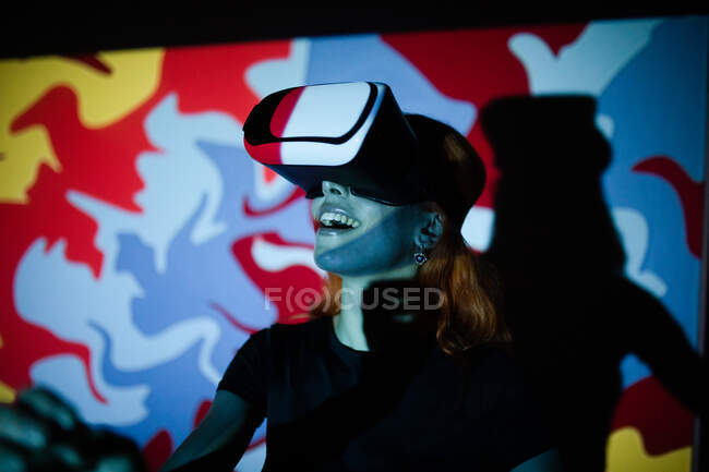Щаслива пані в чорній футболці, стоячи в кімнаті з яскравими вогнями і з використанням VR навушників — стокове фото