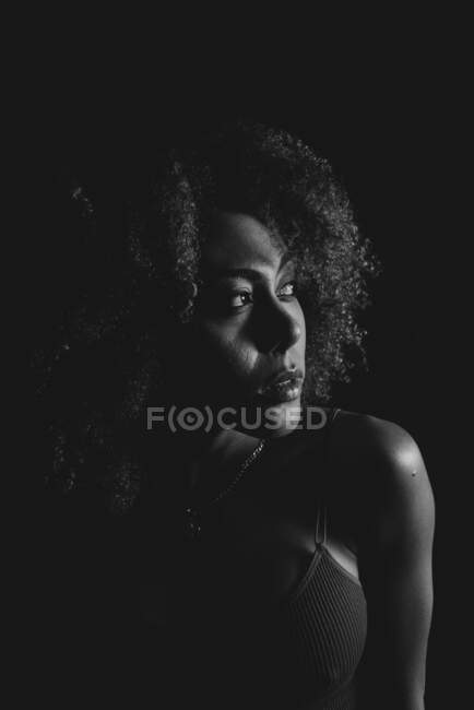 Black and white charming African American female model with curly hair looking away in dark studio — Stock Photo