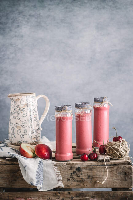 Milkshake refrescante com nectarinas e cereja servida em copos em mesa de madeira com flores — Fotografia de Stock