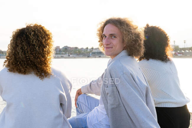 Lächelnder Mann chillt mit Freundinnen am Stadtdamm und blickt über die Schulter in die Kamera — Stockfoto