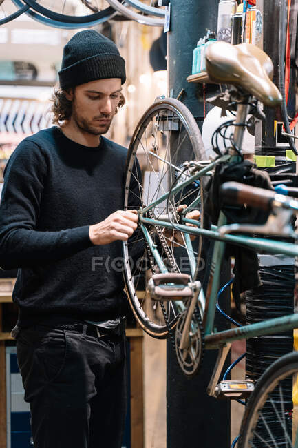 Vista lateral da roda de reparação mecânica masculina grave da bicicleta enquanto trabalhava na oficina — Fotografia de Stock