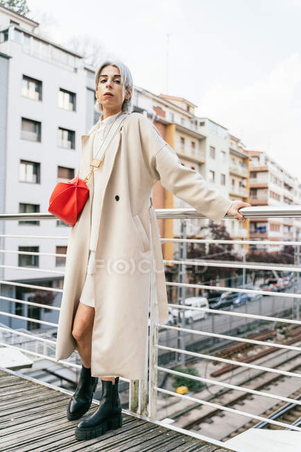 Самозабезпечена трансгендерна жінка в стильному пальто, стоячи на мосту і дивлячись на камеру — стокове фото