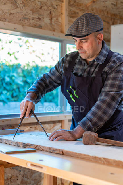 Lenhador masculino usando bússola profissional ou divisor enquanto marca prancha de madeira na bancada na oficina de carpintaria — Fotografia de Stock