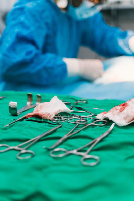 Набор различных хирургических инструментов и окровавленных салфеток в операционной ветеринарной клиники во время операции с анонимным врачом урожая, лечащим пациента — стоковое фото