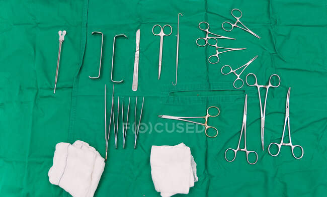 Vista superior de varios suministros quirúrgicos profesionales, incluyendo tijeras y pinzas y vendaje en hoja verde preparado para su operación en el hospital veterinario - foto de stock
