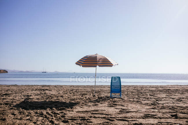 Paisaje vista de sombrilla y silla colocada sobre arena en la playa en un día de verano - foto de stock