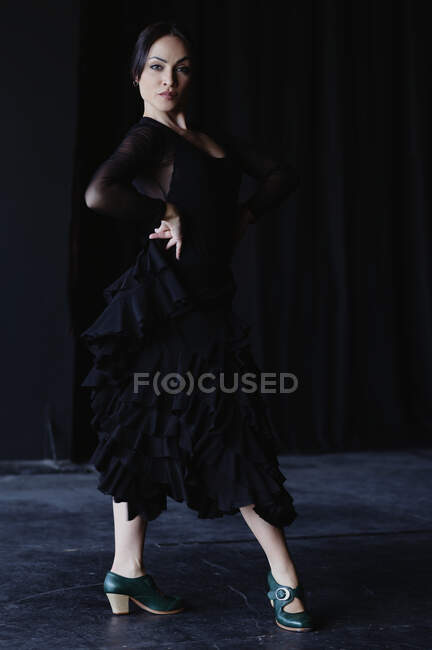 Mujer joven y elegante en traje negro bailando flamenco mientras mira a la cámara - foto de stock