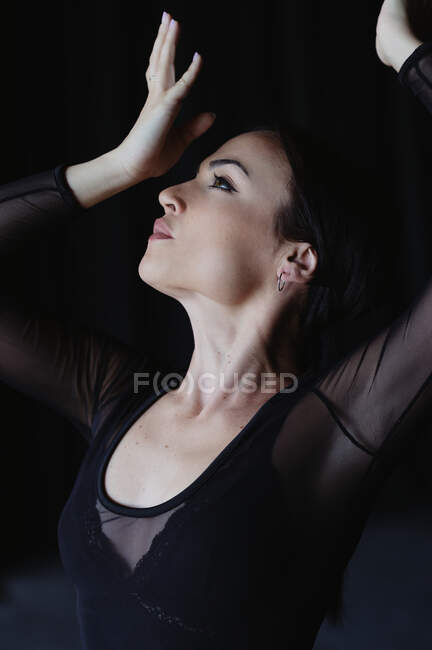 Joven mujer elegante en negro llevar baile flamenco con los brazos levantados mientras mira hacia arriba - foto de stock