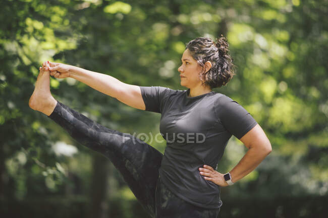 Plump Weibchen mit der Hand auf der Taille stehend in Utthita Hasta Padangushthasana Pose, während sie Yoga praktiziert und sich im Park nach vorne freut — Stockfoto