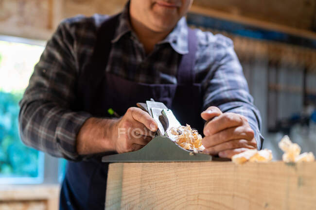 Unrecognizable male woodworker smoothing wooden detail with jack plane while working in professional carpentry workshop — Stock Photo