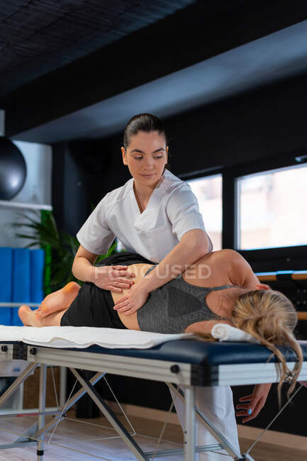 Terapeuta femenina en bata blanca masajeando la espalda de la mujer durante la sesión de osteopatía en la clínica - foto de stock