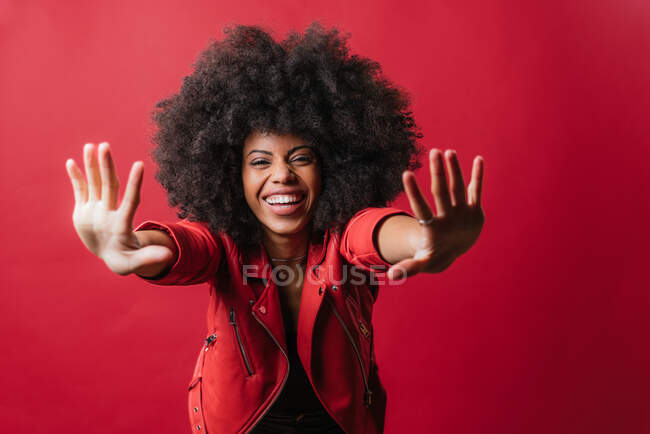 Femme afro-américaine effrayée aux cheveux bouclés montrant un geste d'arrêt sur fond rouge en studio et regardant la caméra — Photo de stock