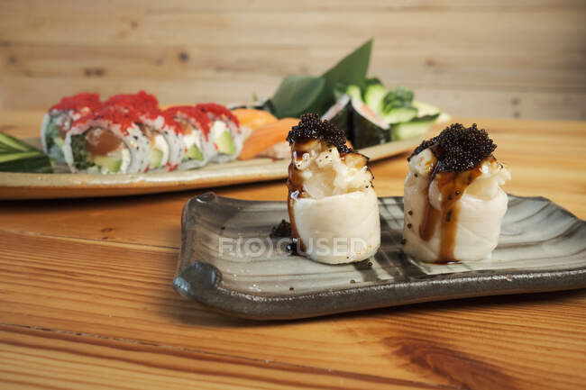 Gunkan sushi and Uramaki rolls served on plates on wooden table in Japanese restaurant — Stock Photo