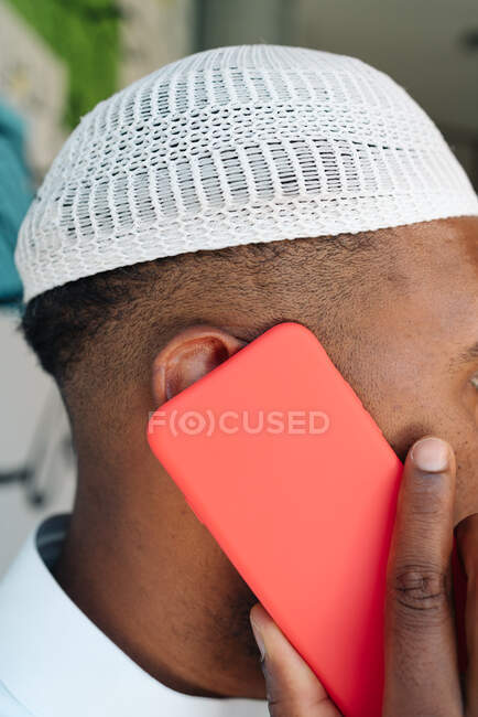 Crop Muslim male in traditional clothes and using cellphone while standing near wall on street — Stock Photo