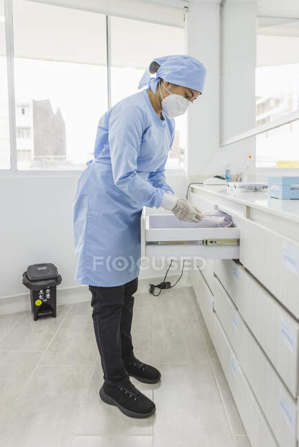 Vista laterale dell'ortodontista donna appoggiata in avanti sopra il cassetto con strumenti medici al lavoro in ospedale — Foto stock