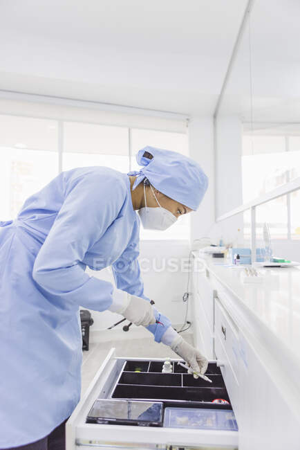 Vista lateral do ortodontista feminino inclinado para a frente acima da gaveta com instrumentos médicos no trabalho no hospital — Fotografia de Stock