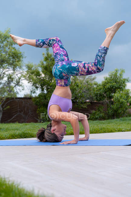 Vista lateral da jovem fêmea em sportswear de pé na cabeça com pernas levantadas enquanto pratica ioga no verão — Fotografia de Stock