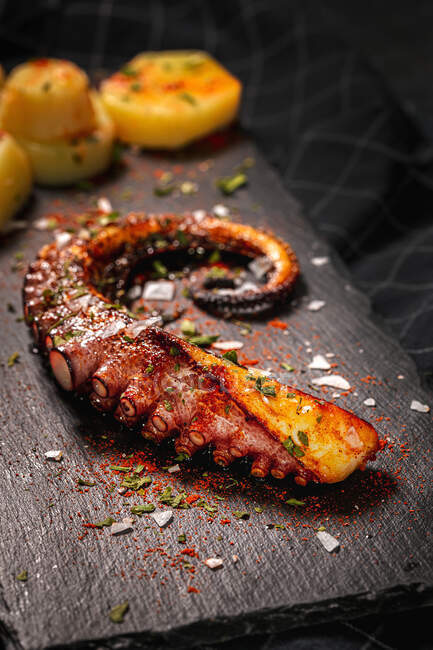 Dall'alto tentacolo di polpo fritto e pezzi di patata serviti con spezie su tavola nera — Foto stock