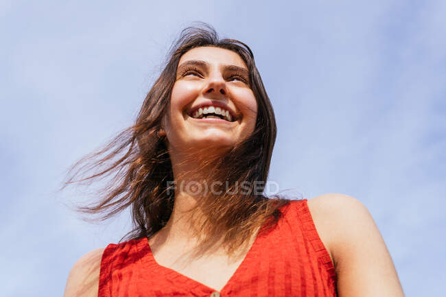 Niedriger Winkel einer fröhlichen Frau, die vor blauem bewölkten Himmel steht — Stockfoto