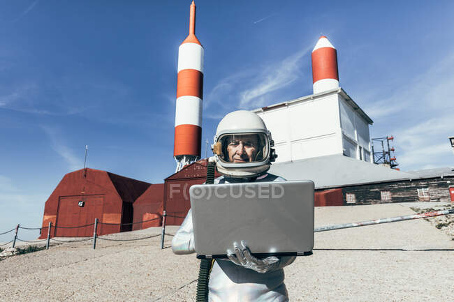 Чоловічий астронавт у скафандрі переглядає дані з нетбука, стоячи надворі з антеною, що має форму ракети. — стокове фото