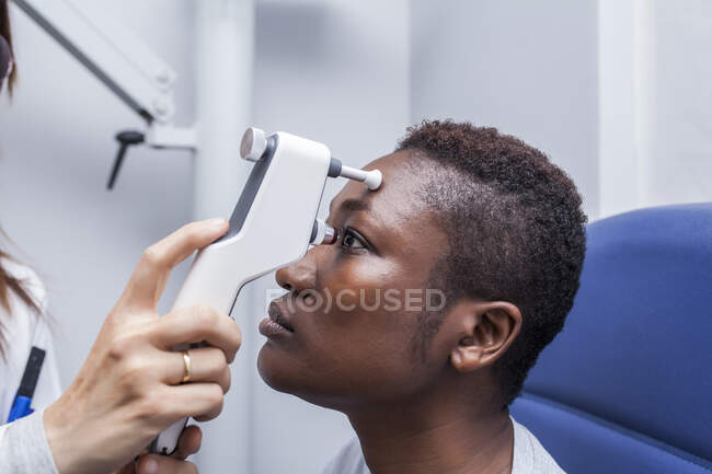 Optometrista usando un oftalmoscopio durante el estudio de la vista de una mujer negra - foto de stock