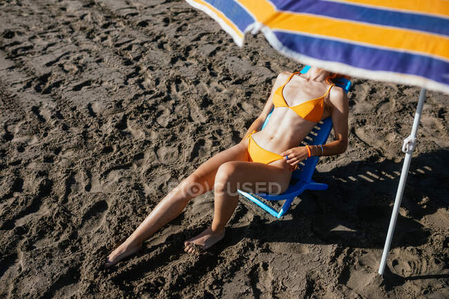Anonyme junge rothaarige Frau sitzt an einem sonnigen Sommertag auf einem Stuhl am Strand — Stockfoto