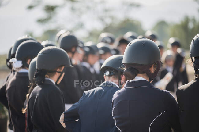 Gruppe anonymer Jockeys mit Helmen steht an einem sonnigen Tag im Pferdeclub auf der Koppel — Stockfoto