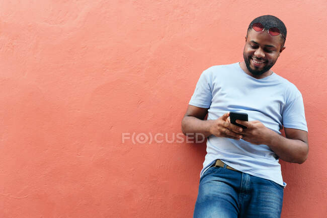 Улыбающийся африканский мужчина смотрит на свой смартфон, стоя в городе — стоковое фото