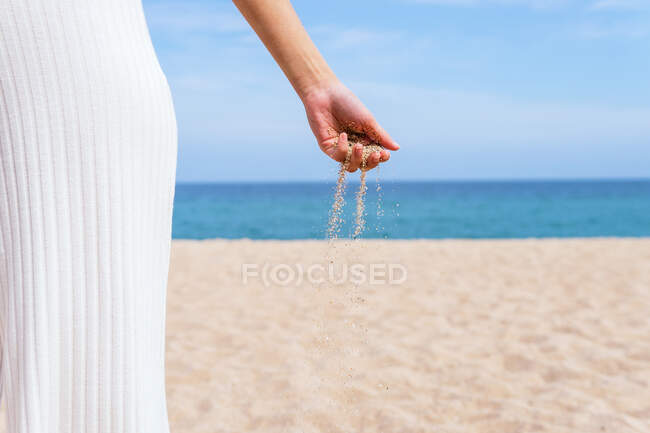 Crop anonymous female with handful of sand running through fingers standing on seashore in summer — Stock Photo