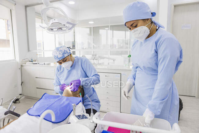 Estomatologista feminina tratando dentes de paciente masculino irreconhecível contra colega de trabalho em uniforme no hospital — Fotografia de Stock