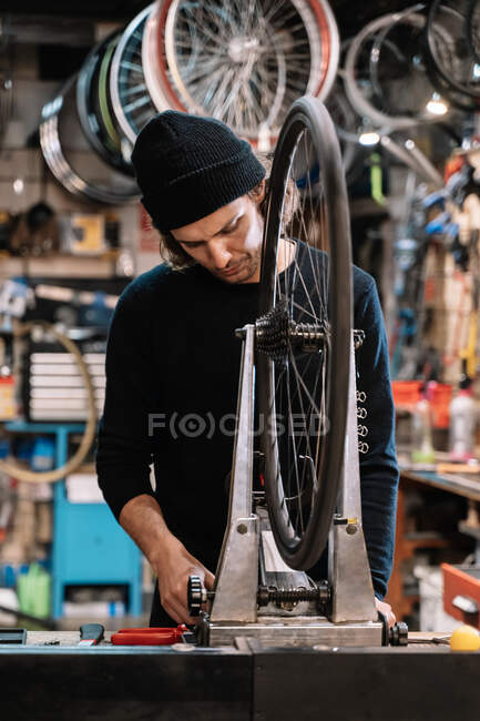 Joven maestro examinando neumático en rueda de bicicleta mientras trabaja en taller de servicio de reparación profesional - foto de stock