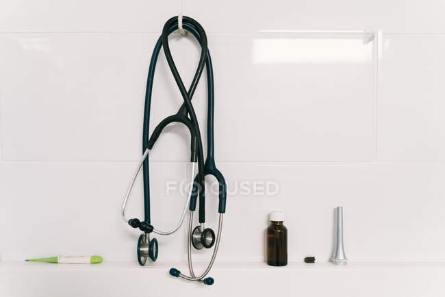 Conjunto de herramientas médicas veterinarias profesionales que incluyen estetoscopio y termómetro con botella de vidrio colocada en soporte blanco en la clínica - foto de stock