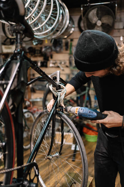 Professional skilled male mechanic using electric screwdriver while installing part of bicycle in workshop — Stock Photo