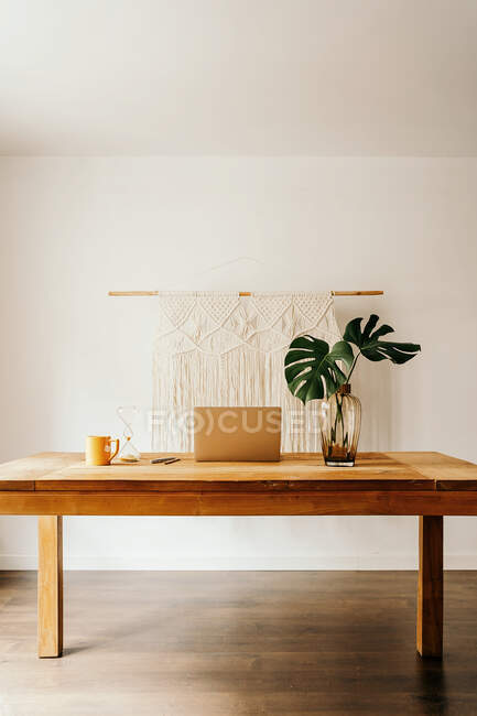 Laptop e smartphone na mesa de madeira com xícara de chá e vaso de vidro com plantas verdes contra a parede branca — Fotografia de Stock