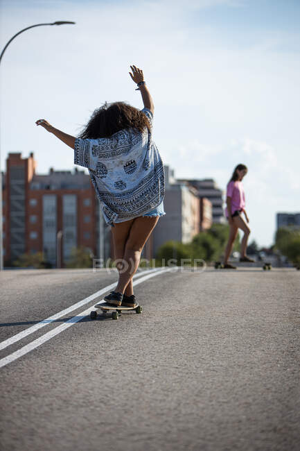 Young and afro woman skating long board by an empty bridge at sunset, back view — Stock Photo